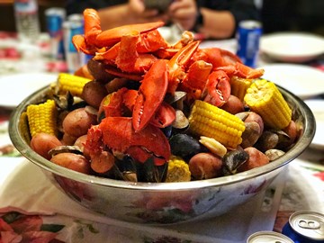 Ingredients for a lobster boil, including corn, potatoes, sausage, and seasoning.